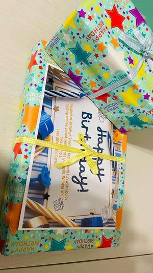 Colorful birthday gift wrap with stars and ribbons around a birthday card and present box