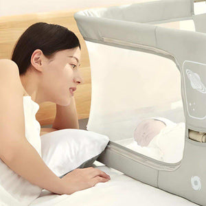 Mother watching baby sleeping safely in NightNest Bedside Rail with breathable mesh barrier