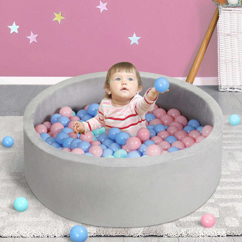 Baby playing in BabiePlay Ultimate Foam Ball Pit with pastel pink and blue balls in a grey foam pit against a pink wall with star decals